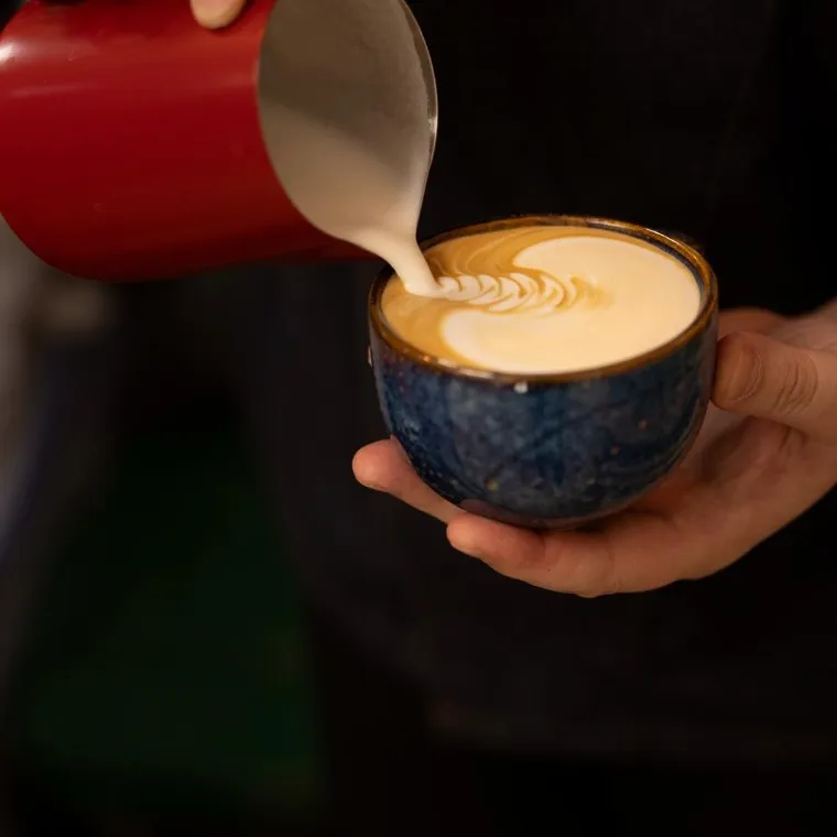 Barista vertiendo leche para un latte art en una taza azul de Brava
